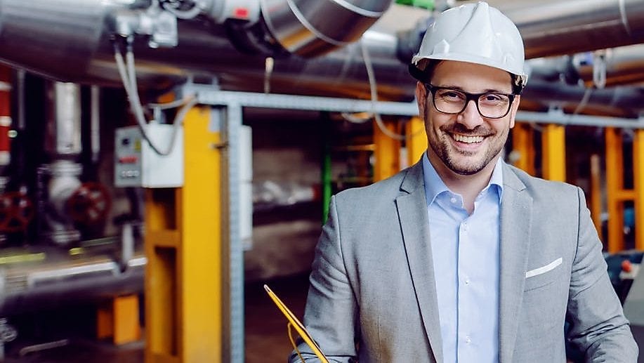 Ein Mann steht mit Helm und Mappe vor einer Industrieheizung
