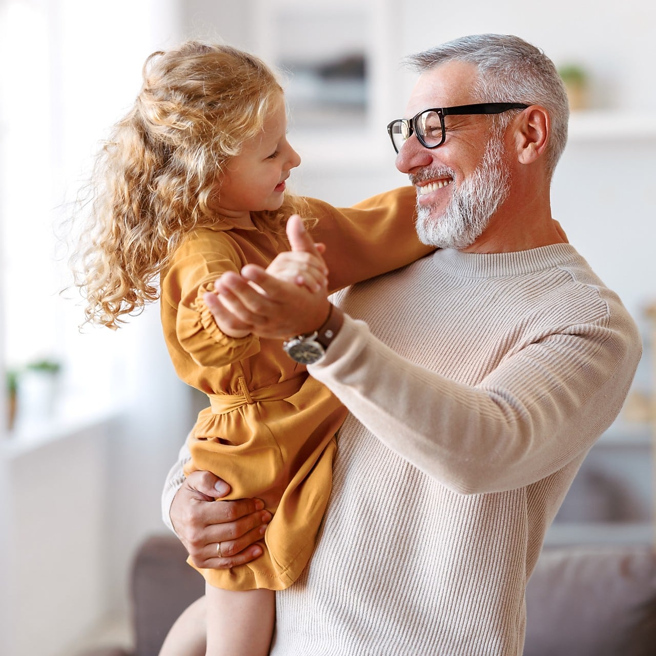 Ein älterer Mann hält ein kleines Kind liebevoll im Arm in einer hellen, freundlichen Umgebung.