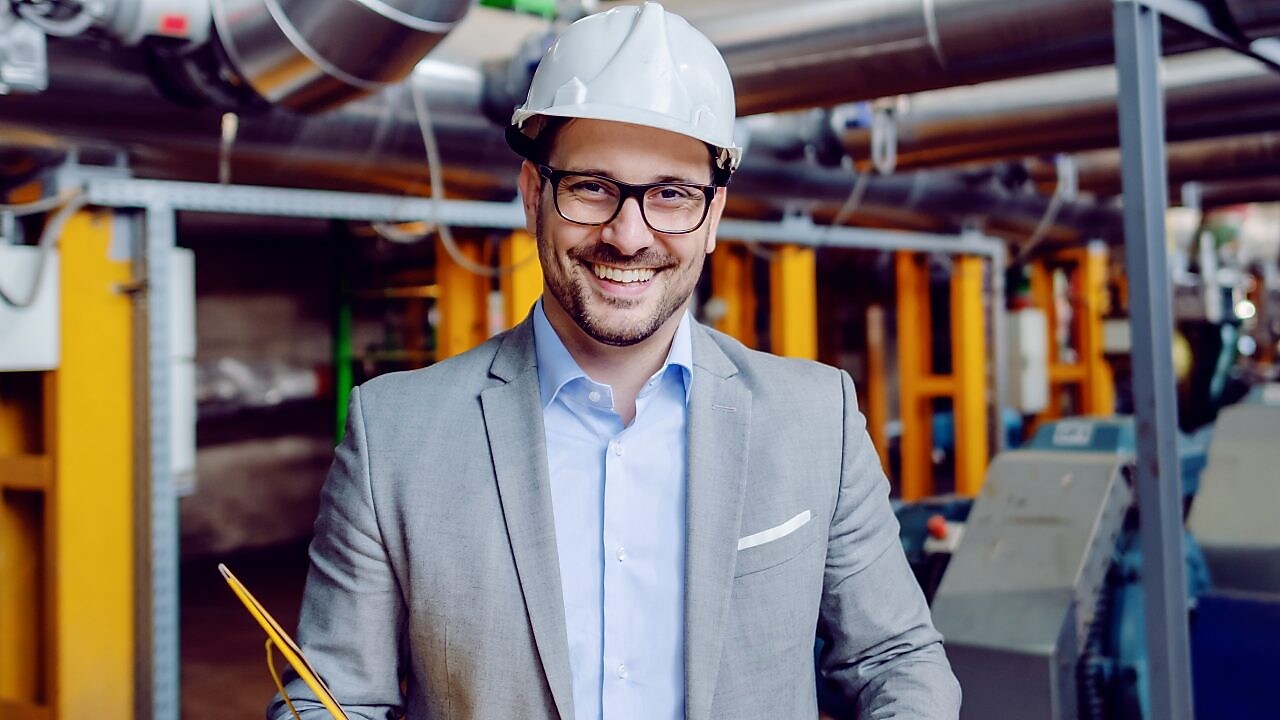 Unternehmer steht vor einer Heizanlage und lächelt