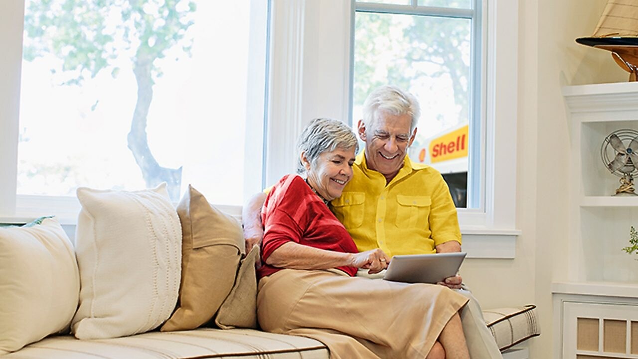 Best Ager Paar sitzt mit Tablet auf der Couch und liest die Shell Heizöl FAQs