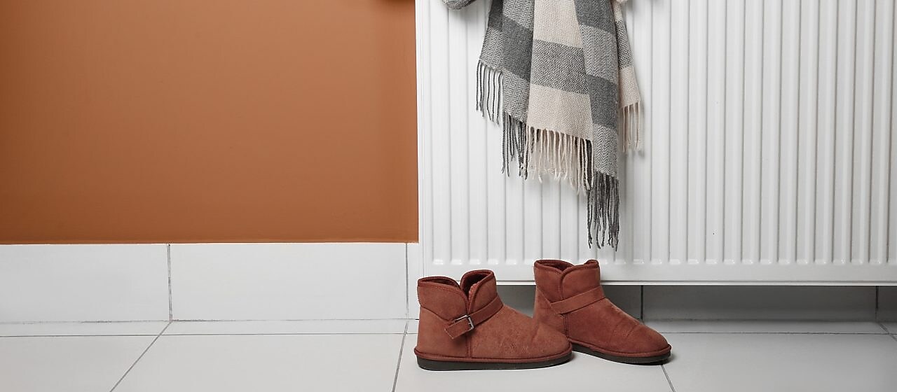 Warme Hausschuhe stehen unter einer Heizung auf den Fliesen.