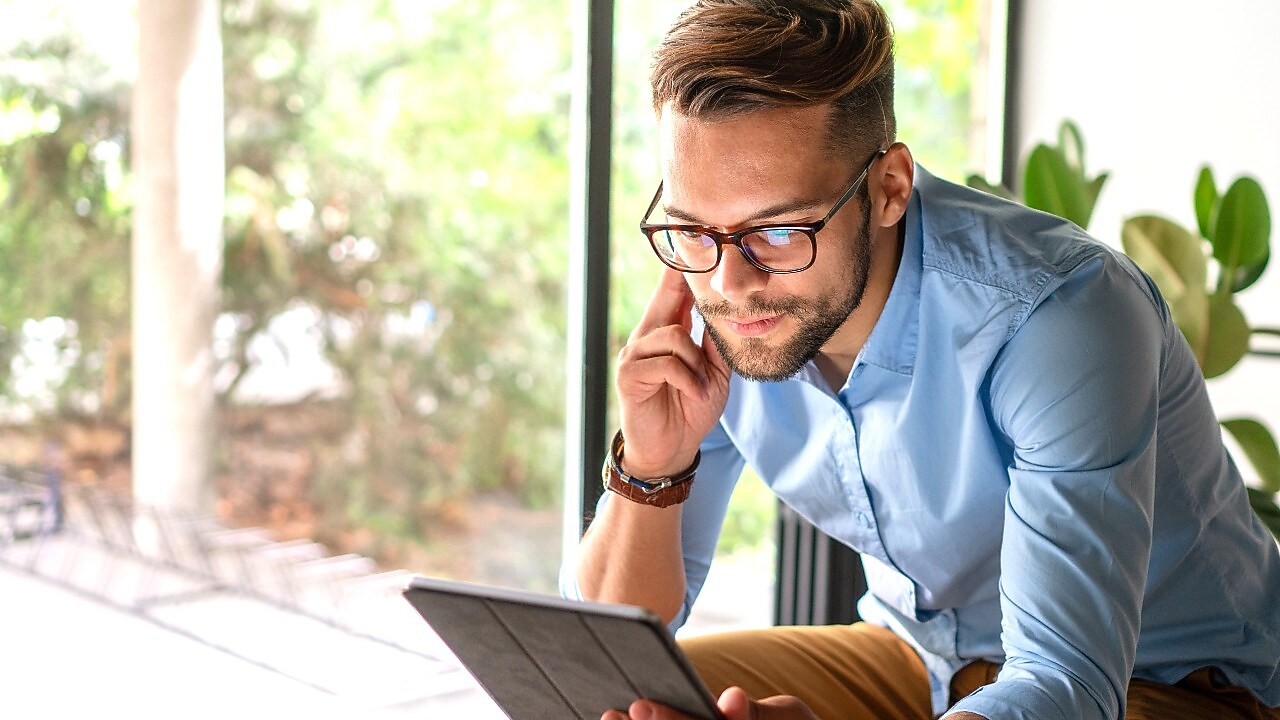Ein Mann guckt auf sein Tablet in seinem Wohnzimmer.
