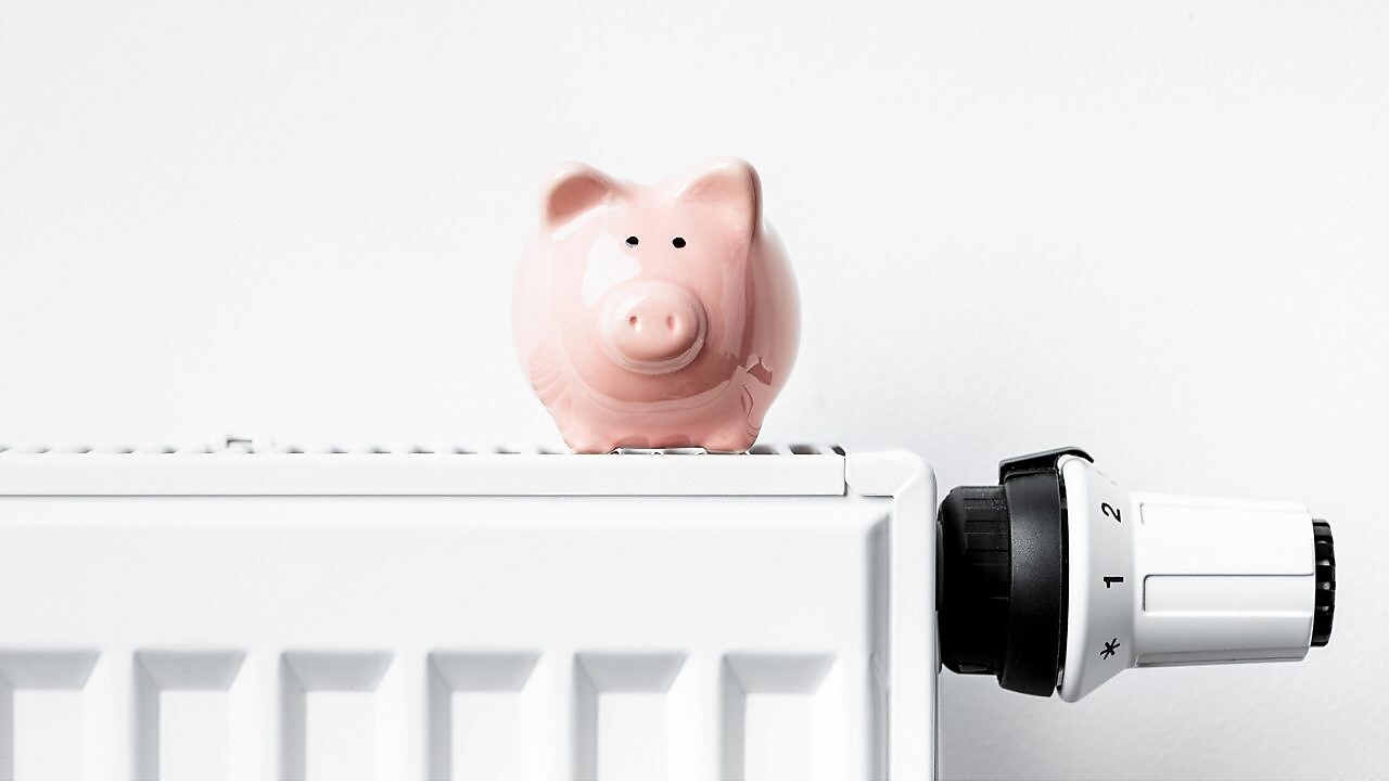 Sparschwein steht auf Heizkörper mit Thermostat