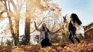 Mutter und Tochter werfen gemeinsam Laub im herbstlichen Garten in die Luft.