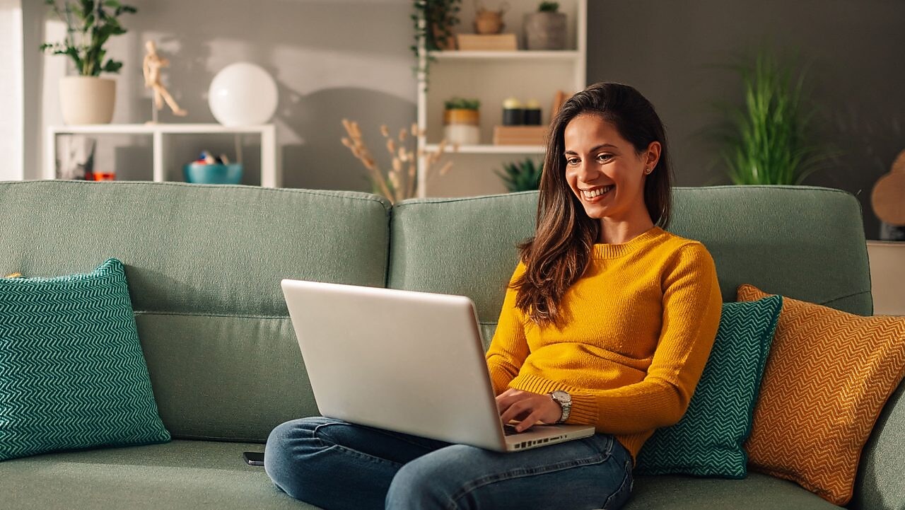 Frau sitzt mit Laptop auf einem mintgrünen Sofa 