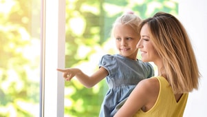 Frau mit kleinem Mädchen auf dem Arm am Fenster zu Hause