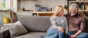 Ein Paar sitzt auf dem Sofa und lacht. Der Raum sieht warm und gemütlich aus.