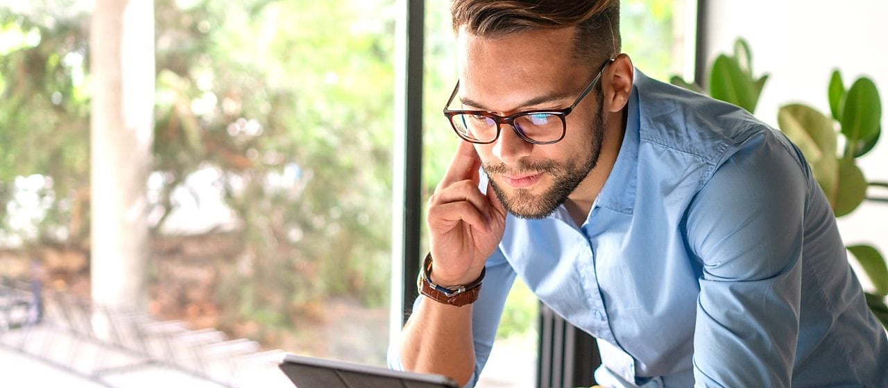 Ein Mann guckt auf sein Tablet in seinem Wohnzimmer.