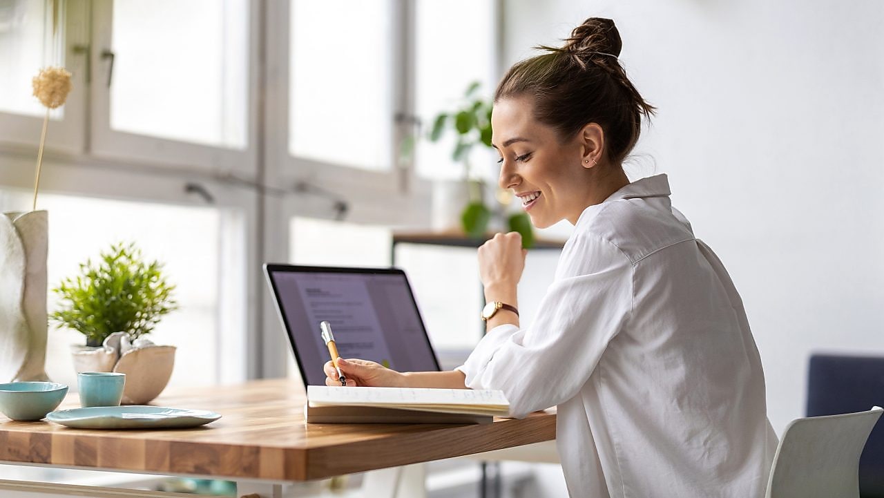 Frau sitzt vor einem Laptop und schreibt auf einen Zettel.
