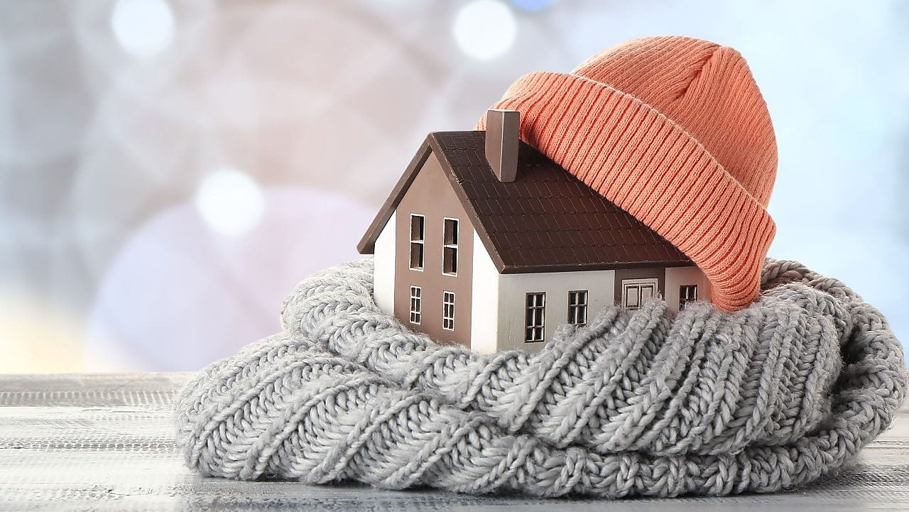 Abbildung eines Hauses in warmer Kleidung auf einem Tisch vor verschwommenen Lichtern.