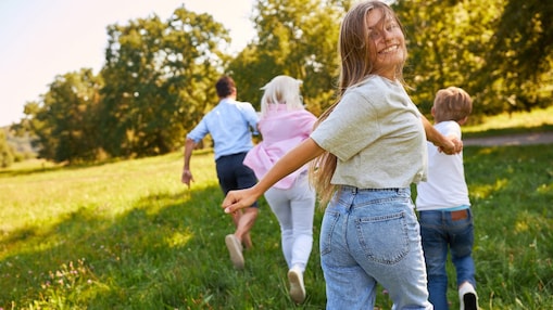 Eine Familie rennt zusammen über eine Wiese in die Sonne.