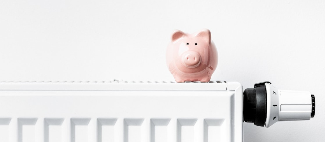 Sparschwein steht auf Heizkörper mit Thermostat
