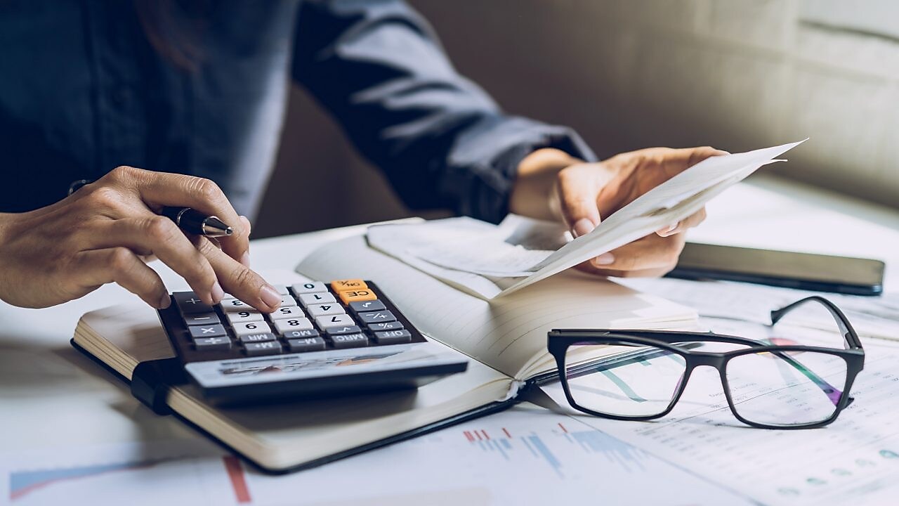 Hände mit Stift und Taschenrechner auf Buch mit Brille