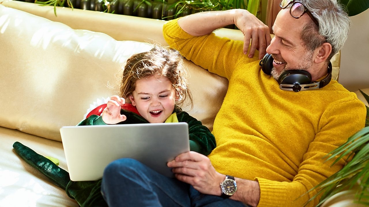 Mann mit Kind und Laptop auf Sofa