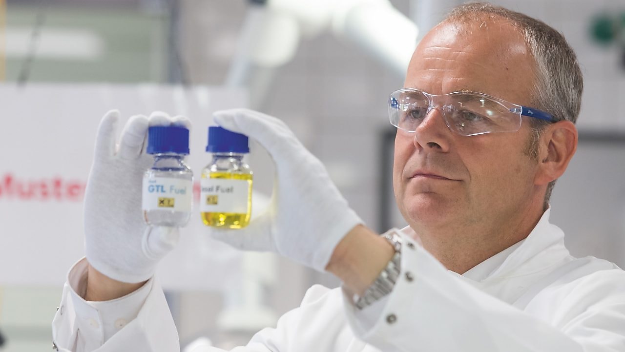 Ein Labormitarbeiter hält zwei Probefläschchen hoch und vergleicht deren Inhalt.