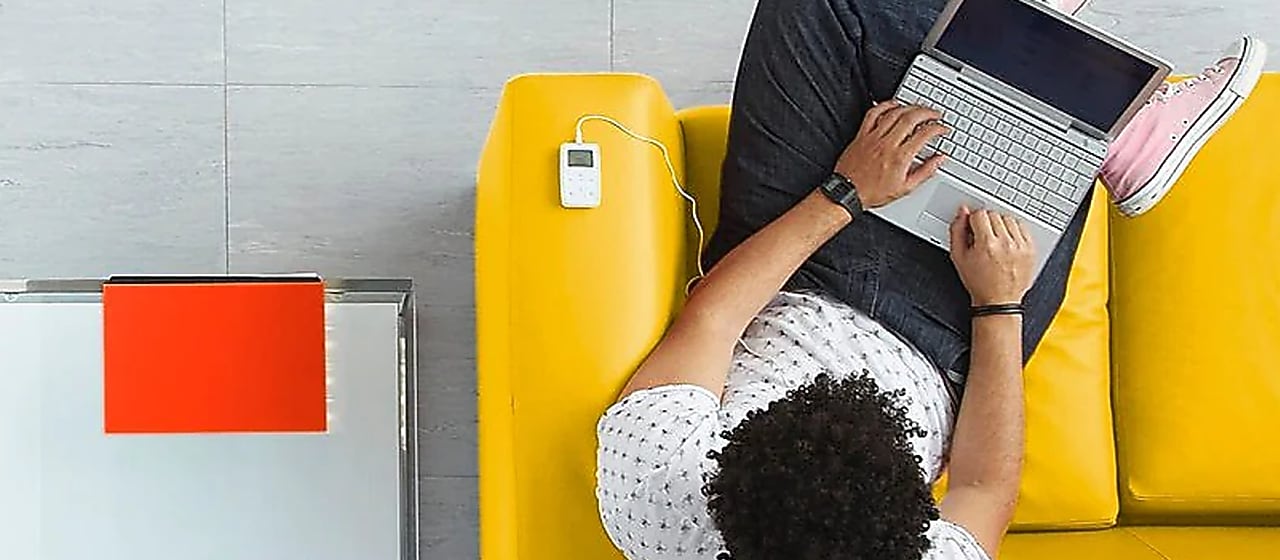 Vogelperspektive: Mann sitz mit Laptop auf dem Schoß auf einem gelben Sofa