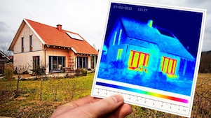Thermoscan in Hand mit gesamter Hausansicht im Hintergrund
