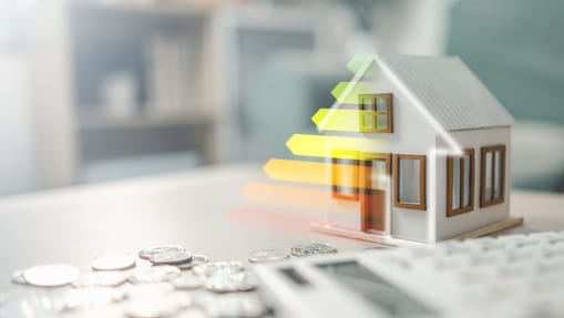 Energieeffizienzklasse eines Wohngebäudes, dargestellt durch ein Musterhaus mit Taschenrechner und Münzen für Energiebilanz, Kosteneinsparungen und nachhaltiges Wohnen.