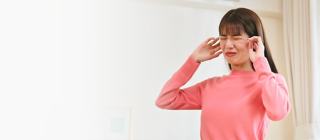 Frau die das Gesicht verzieht und sich die Ohren zuhält