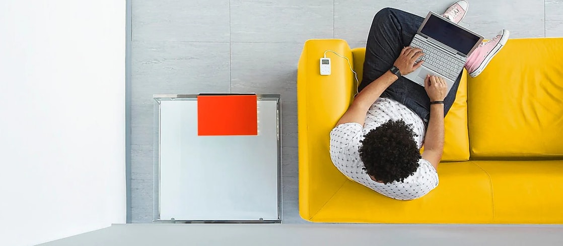 Vogelperspektive: Mann sitz mit Laptop auf dem Schoß auf einem gelben Sofa