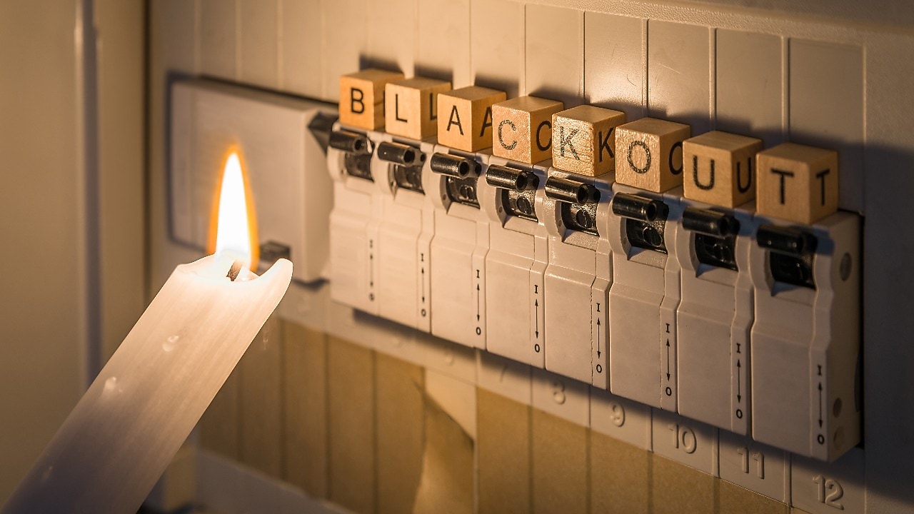 Verteilerkasten mit Sicherungen bei Stromausfall, beleuchtet von weißer Kerze, Blackout-Schriftzug