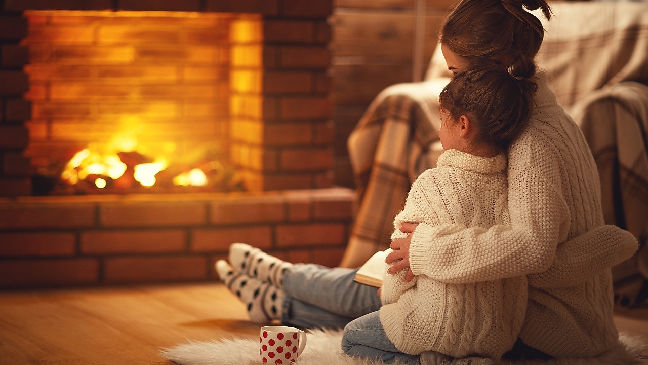 Mutter und Tochter umarmen sich und genießen sitzend die Wärme am Kamin