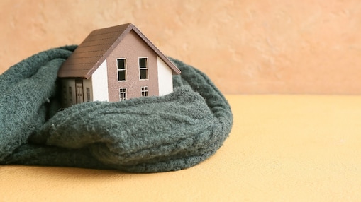 Modell eines Hauses mit warmem Schal umwickelt auf beigem Hintergrund