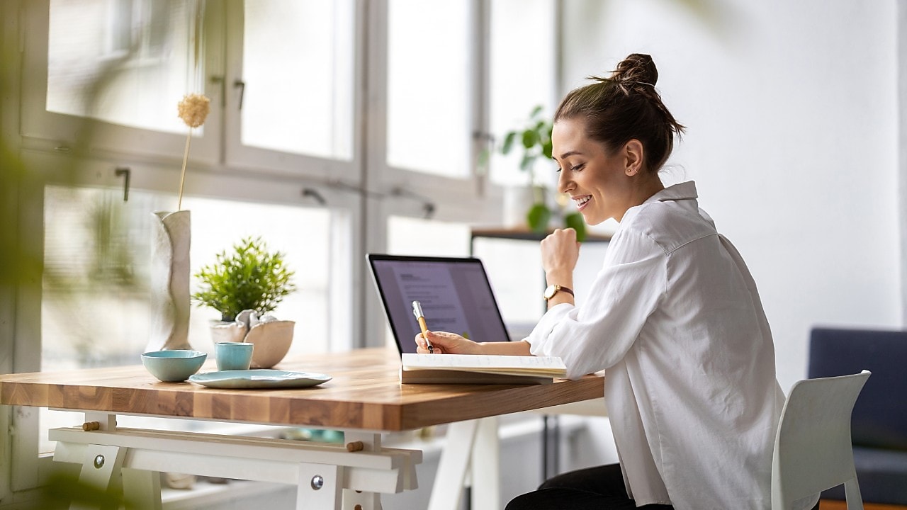Frau sitzt vor einem Laptop und schreibt auf einen Zettel.