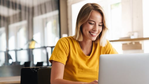 Junge Frau blickt lächelnd in Ihr Notebook