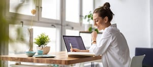 Frau sitzt vor einem Laptop und schreibt auf einen Zettel.
