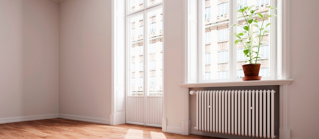 Eine leere Altbauwohnung mit Balkon und Heizung unter dem Fenster und einer Pflanze auf dem Fensterbrett.