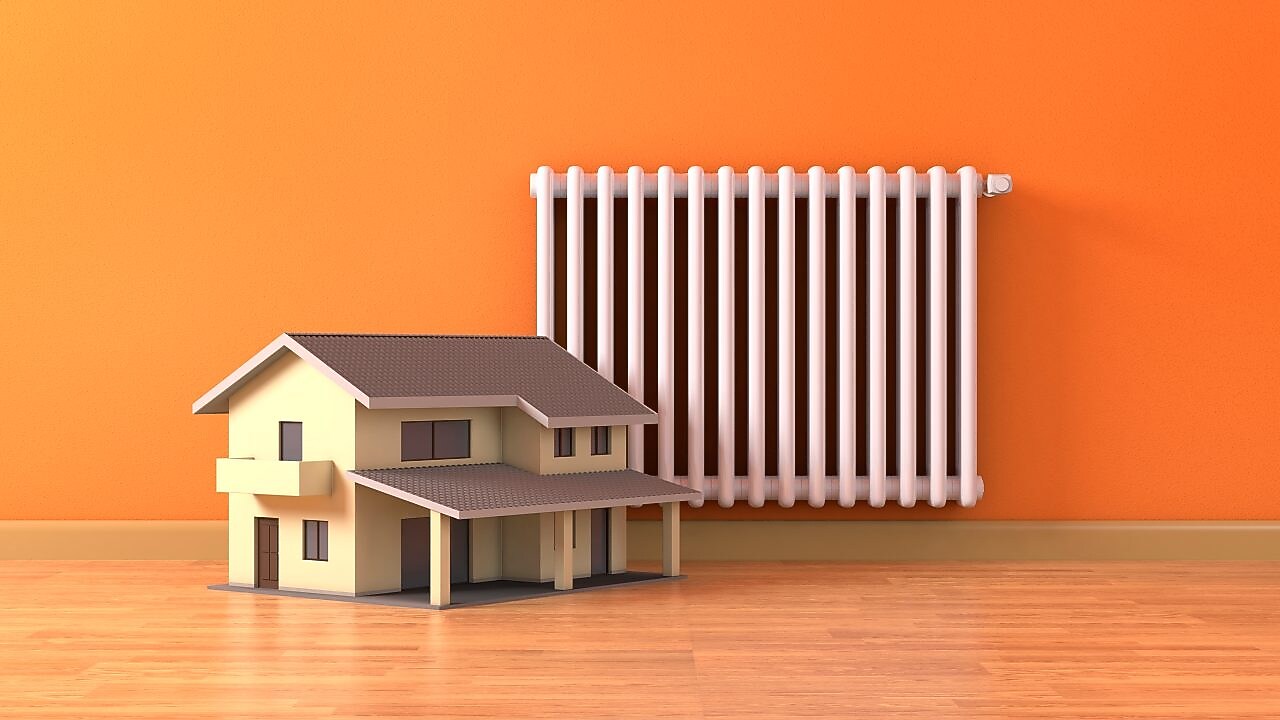 Ein Modellhaus steht vor einer orangefarbenen Wand, an der eine Heizung montiert ist.