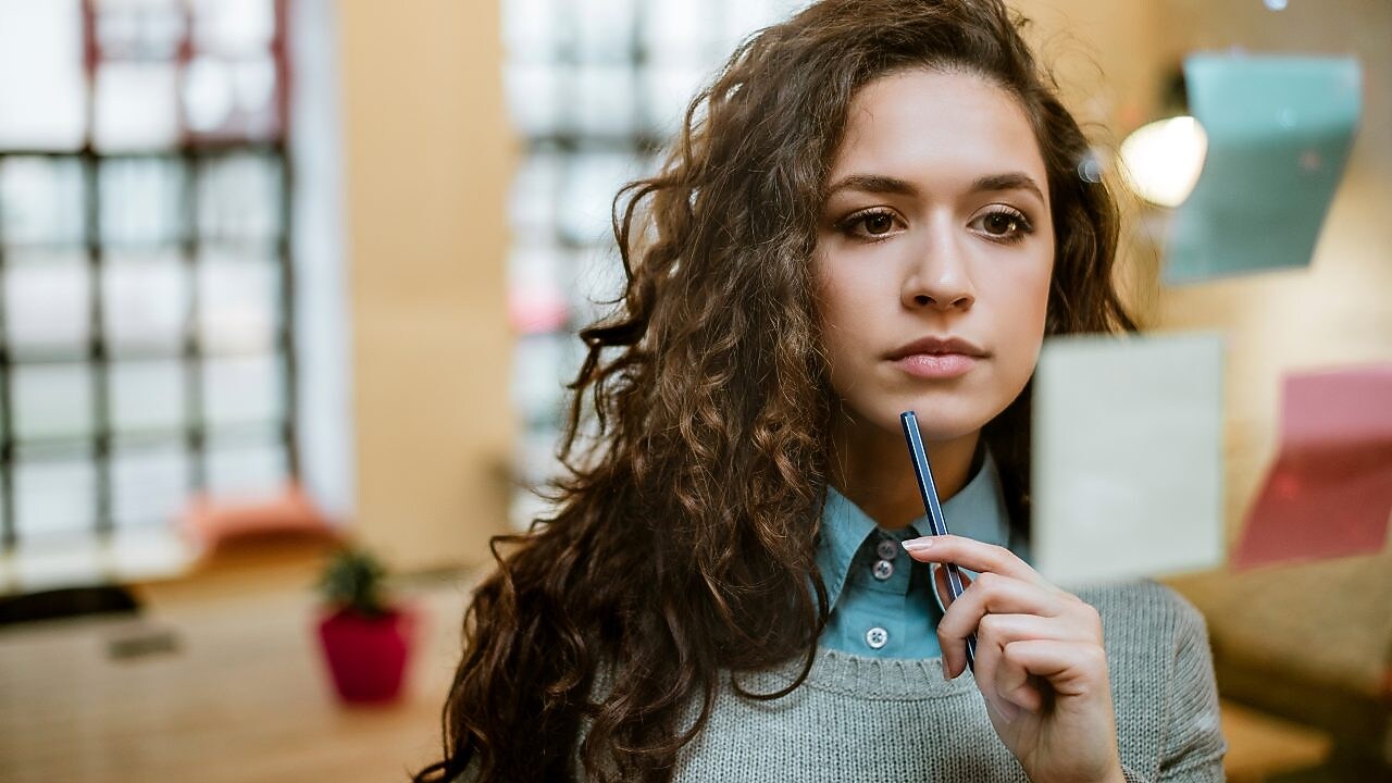 Eine Junge Frau schaut sich ihre Post-its an und überlegt.