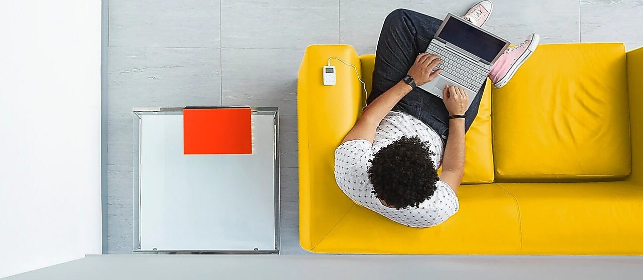 Vogelperspektive: Mann sitz mit Laptop auf dem Schoß auf einem gelben Sofa