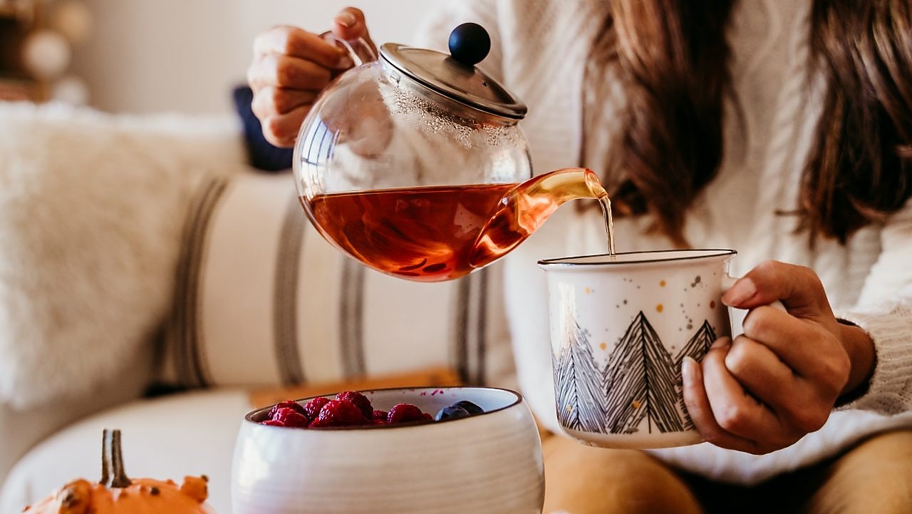 Frau, sitzt auf dem Sofa, schenkt Tee in eine Tasse ein