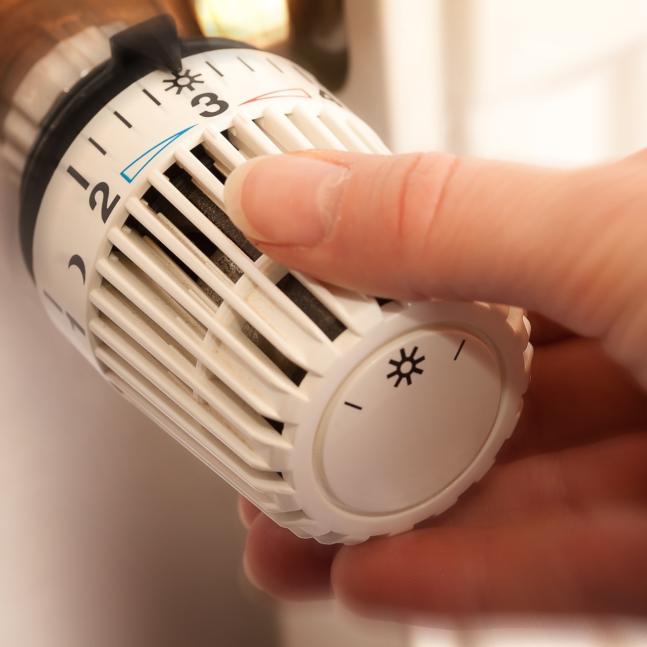 Hand dreht manuell am Temperaturregler an der Heizung