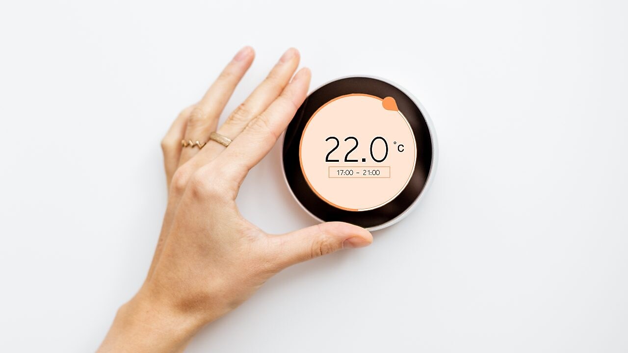 Eine Frauenhand stellt Raumtemperatur an einem modernen Thermostaten ein