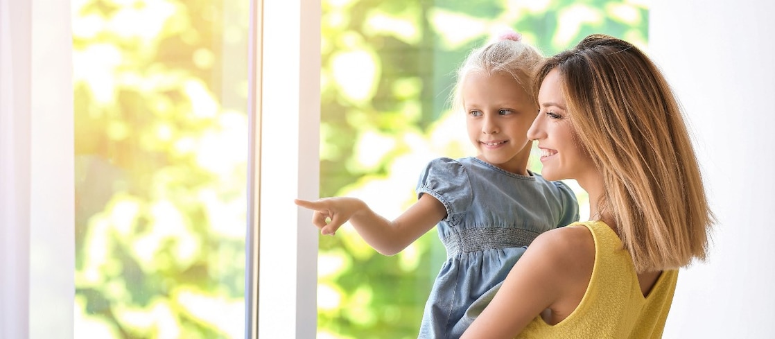 Frau mit kleinem Mädchen auf dem Arm am Fenster zu Hause