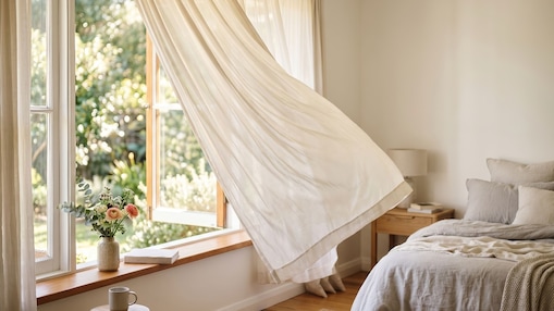 Helles Schlafzimmer mit offenem Fenster und wehenden Vorhängen