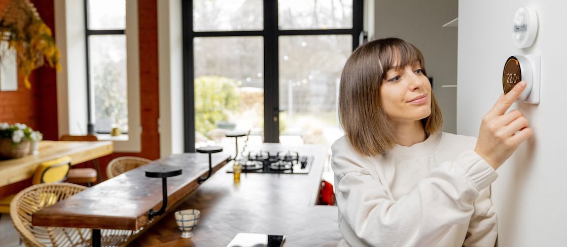 Frau reguliert die Temperatur in ihrer Wohnung mithilfe eines elektronischen Thermostats