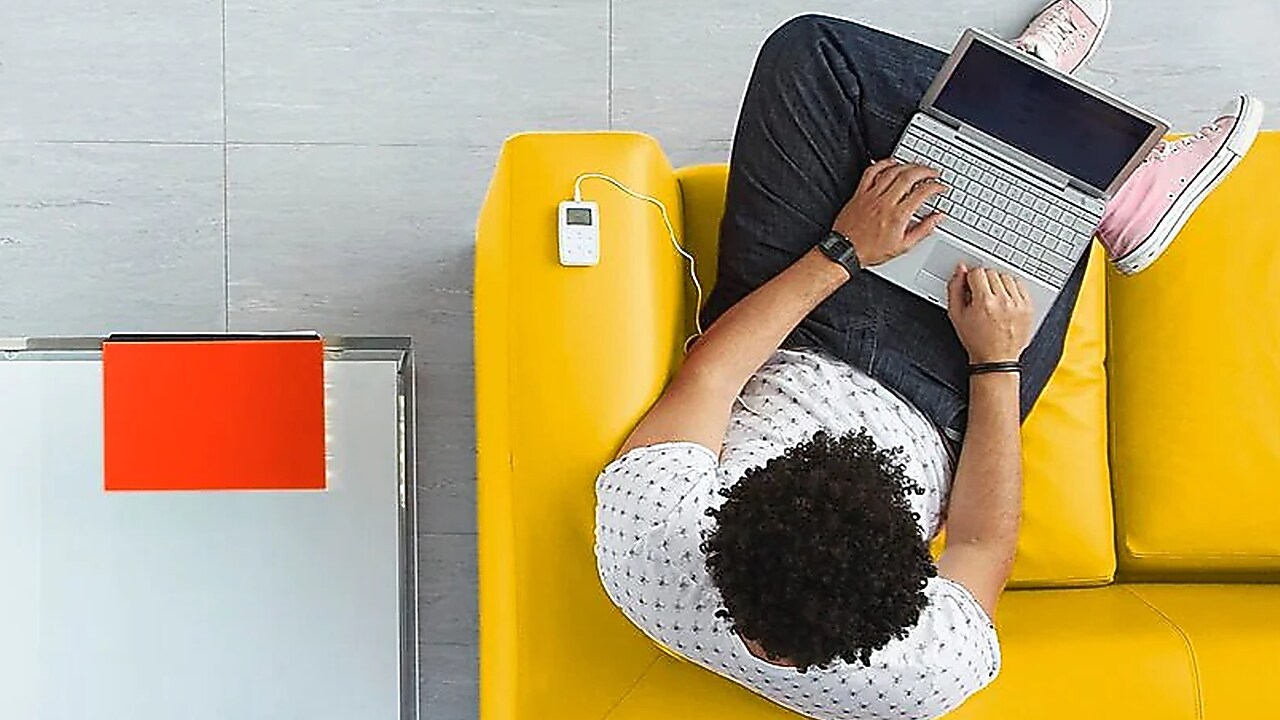 Vogelperspektive: Mann sitz mit Laptop auf dem Schoß auf einem gelben Sofa