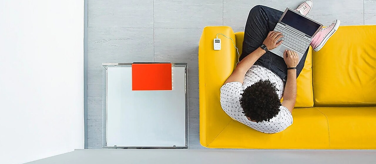 Vogelperspektive: Mann sitz mit Laptop auf dem Schoß auf einem gelben Sofa