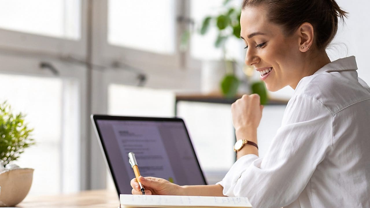 Frau am Schreibtisch mit Laptop, Notizbuch und Stift