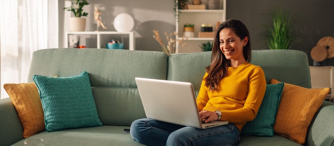 Frau sitzt mit Laptop auf einem mintgrünen Sofa