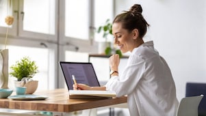 Frau sitzt vor einem Laptop und schreibt auf einen Zettel.