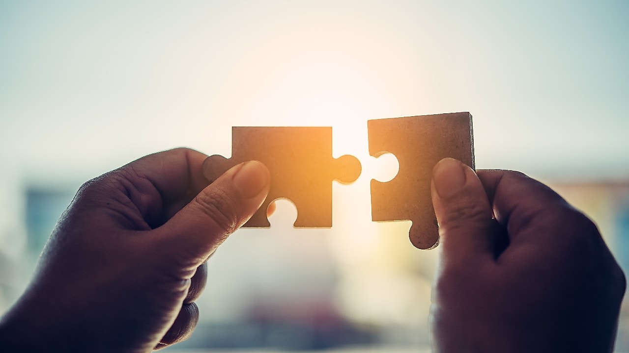 Zwei Puzzleteile werden mit zwei Händen gegen die Sonne gehalten.