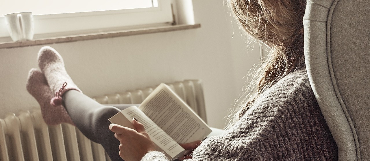 Ein Mann, Frau und ein Kind sitzen in einem Haus, halten sich ein Karton über den Kopf, das aussieht wie ein Dach. Die Sonne scheint hindurch.