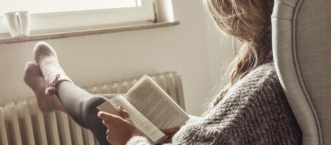 Ein Mann, Frau und ein Kind sitzen in einem Haus, halten sich ein Karton über den Kopf, das aussieht wie ein Dach. Die Sonne scheint hindurch.