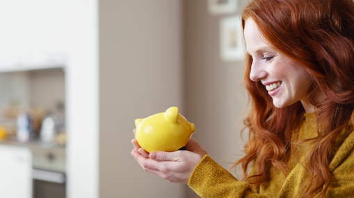 Frau hält ein gelbes Sparschwein in der Hand und schaut es lächelnd an.