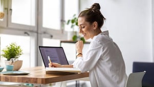Frau sitzt vor einem Laptop und schreibt auf einen Zettel.